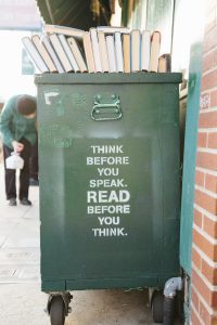 short fiction versus long: dumpster with books on top, sign on side says "think before you speak. READ before you think."